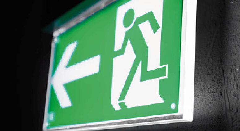 Green emergency exit sign with a running figure and an arrow pointing left.